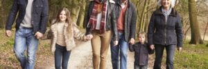 Six people, including two children, walk together on a wooded path during daytime, dressed in casual winter clothing.