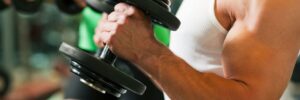 Two people lifting dumbbells in a gym, focusing on arms and hands holding the weights.